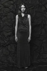 Vestido largo de fiesta confeccionado con hilo metalizado color marrón. Tiene cuello halter con lazada, escote drapeado, espalda descubierta con tira ajustable y cierre lateral con cremallera oculta.