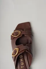 Sandalias planas de cuero color marrón con dos tiras anchas sobre el empeine, cada una con hebilla dorada.