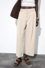 Pantalón color beige de tiro alto, corte ancho y largo midi, con pinzas delanteras, bolsillos laterales y traseros. Cierre frontal con cremallera y botón.