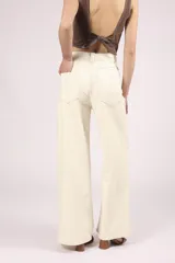 Pantalón de jean color crudo, de corte palazzo y tiro alto, con bolsillos delanteros y traseros, y costuras a la vista.