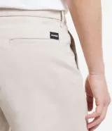 Bermuda de hombre, modelo loose con corte de sastrería, confeccionada en sarga de algodón y elastano. Color beige claro, con cierre de botón y cremallera, bolsillos y bajo ancho.