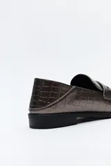 Mocasines color peltre con textura símil cuero de cocodrilo, punta cuadrada, detalle de bordado a tono en la capellada y taco bajo.