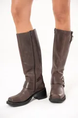 Bota biker de caña alta color marrón, con hebilla en la parte superior y aro en la parte inferior, fabricada en cuero.