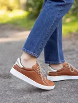 Zapatillas acordonadas de cuero color marrón con detalles dorados en el talón y suela blanca.