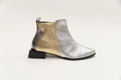 Botín corto de cuero color bronce con detalle de pieza de cuero charolada negra en el talón, cierre lateral y taco geométrico.