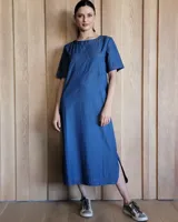 Vestido midi negro con cuello redondo y mangas cortas. Presenta dos bolsillos cuadrados en el pecho y ribetes blancos en cuello, mangas, bolsillos y ruedo.