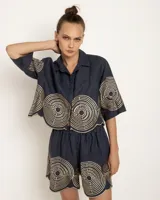 Camisa azul marino de lino con bordado dorado en forma de laberinto, de corte holgado y mangas cortas.