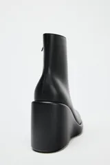 Botín negro de cuero sintético con plataforma y tacón de cuña. Cierre mediante cremallera lateral y acabado en punta redonda.