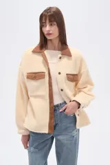 Campera estilo camisa (shacket) de tejido tipo borrego o sherpa color crema, con cuello y tapeta de pana marrón. Posee dos bolsillos frontales con tapa y botones a presión.