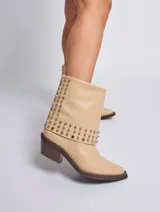 Bota corta color beige con puntera en punta y taco de madera. Presenta apliques de tachas plateadas en el borde superior. Confeccionada en cuero genuino.