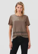 Remera color beige con cuello redondo y mangas cortas con frunce. Presenta una banda horizontal de encaje en el frente.