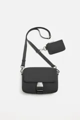 Bandolera negra de tela técnica con correa ajustable y extraíble. Tiene un compartimento principal con cierre de cremallera, un bolsillo interior con cremallera, un bolsillo frontal con solapa y hebilla de liberación rápida, y un monedero removible.
