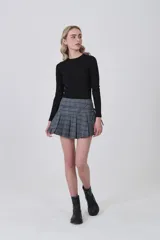 Falda corta plisada de poliéster con estampado tartán en tonos grises, azules y beige. Presenta un detalle de lazo o fajín anudado en la cintura.