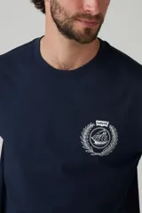 Remera azul marino de corte recto y mangas cortas, con cuello redondo y estampado en el pecho con un logo de un velero dentro de una corona de laureles.