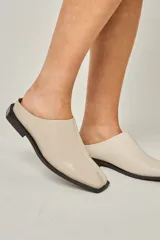 Zuecos color beige confeccionados en cuero vacuno, con punta cuadrada y suela plana color negro.