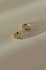 Par de aros tipo argolla dorados con dije de piedra natural con patrón de manchas negras sobre fondo blanco.