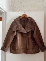 Campera marrón de gamuza sintética con cuello, puños y ruedo de piel sintética color marrón claro. Tiene cierre cruzado con cremallera y bolsillos laterales con cremallera.