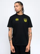 Remera negra de manga corta con cuello redondo y dos escudos amarillos estampados en el pecho: uno con un balón de fútbol rodeado de laureles y otro con un escudo a rayas verticales y estrellas.