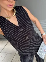 Conjunto de chaleco y pantalón negro con finas rayas verticales blancas. El chaleco es entallado, con escote en V y cierre frontal con botones. El pantalón es de corte palazzo.