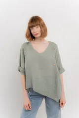 Blusa verde oliva de lino, con escote en V, mangas cortas con vuelta y terminación asimétrica. Presenta una fila de botones decorativos en uno de los hombros.