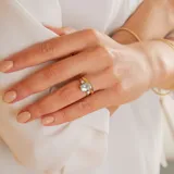 Anillo solitario de oro blanco 18k con aguamarina central ovalada y brillantes laterales engarzados en 4 puntas. El ancho de la banda es de 2,4 mm.