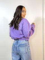 Campera lila con textura capitoneada, cuello camisero, cierre frontal con botones y bolsillos de parche con solapa en el pecho. Tiene elástico en puños y cintura.