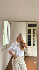 Remera blanca de algodón con cuello tipo bote y detalle de elástico en los hombros, creando un efecto de caída asimétrica.