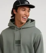 Hoodie masculino de algodón y poliéster, color verde salvia, con capucha ajustable, bolsillo canguro y estampado en el pecho y en la manga izquierda con texto.