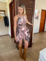 Conjunto de dos piezas compuesto por un top corto de tirantes finos y una minifalda cruzada con lazo, ambos con estampado abstracto en tonos malva, blanco y gris.