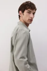 Camisa manga larga color verde oliva, de corte recto, con cuello inglés, tapeta clásica, canesú en la espalda, bolsillo superior abierto, cierre ajustable de botón en los puños y bajo redondeado.