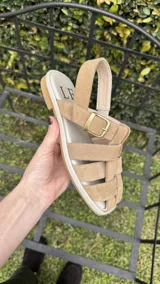 Sandalias de cuero marrón con diseño de tiras entretejidas y hebilla lateral.
