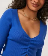 Blusa cropped azul de punto acanalado con escote en V, mangas largas y fruncido frontal.