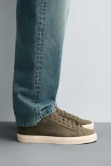 Zapatillas urbanas grises de caña baja, con cordones, puntera redondeada, forro interior en contraste y suela con ligera textura.