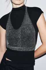 Top plateado de anillas metálicas con cuello halter y hombros descubiertos. Se cierra con mosquetón en cuello y espalda.