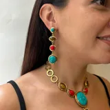 Collar corbatero de bronce con piedras naturales engarzadas. El diseño central presenta una piedra turquesa ovalada, flanqueada por piedras rojas y piedras ojo de tigre ovaladas. De esta piedra central cuelga una cascada de piedras rojas y ojo de tigre engarzadas en marcos de bronce.