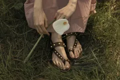 Sandalias marrones tipo ojotas con apliques de tachas doradas y ajuste con hebilla en el talón.