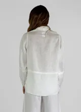 Chaqueta azul de lino con cuello camisero, cierre frontal con botones, mangas largas con puños abotonados, dos bolsillos de parche en el pecho y bajo con terminación desflecada.