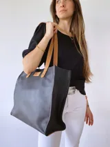 Bolso tipo tote bag de cuero negro con forro de tela, doble asa de cuero color suela, bolsillo frontal y bolsillo interno.