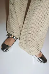 Zapato bailarina plateado con efecto metalizado, acabado en punta redonda y tira con cierre mediante hebilla metálica. Suela de 1,5 cm de altura.