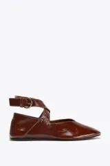Zapato tipo bailarina color marrón, con efecto acharolado, punta redonda y cierre mediante tira con hebilla al tobillo.