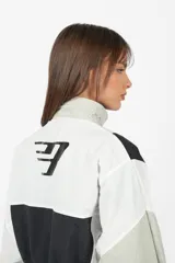Buzo rompevientos anorak gris, de cuello alto, silueta boxy fit, con elástico en terminación de cintura y mangas. Detalle de recortes a contratono. Cierre centrado en delantero de acceso. Bolsillo con tapa por debajo, con cierre escondido. Tancas en cuello con elástico en su contorno, por interior. Estampa en lateral derecho, y centrado en espalda.