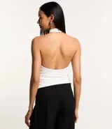 Blusa blanca sin mangas con cuello alto halter, botón en la parte de atrás del cuello, fruncidos laterales y efecto brilloso.