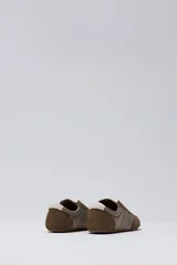 Zapatilla tipo slip-on de caña baja, con capellada combinada en tonos marrón oscuro (capellada y puntera de gamuza) y beige acolchado (zona central). Posee un pequeño detalle en blanco en el talón.