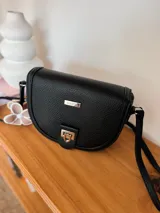 Bandolera negra de cuero sintético con textura granulada, forma de media luna, cierre con broche metálico dorado y correa larga ajustable.