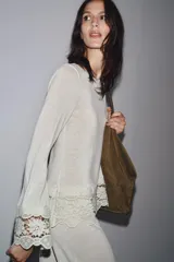 Camiseta blanca de manga larga con cuello redondo y detalle de encaje en el ruedo y puños.