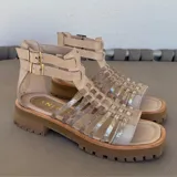 Sandalias bajas de cuero color beige con tiras horizontales plateadas y cierre con hebilla al tobillo.