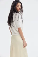 Pollera midi color crema, con leve brillo y caída suave. Modelo de tiro alto con elástico oculto en la cintura y leve vuelo en el bajo.