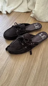 Mocasines tipo mule color beige, con detalle de cordones y ojales metálicos.