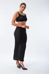 Conjunto de top y falda de tejido de punto calado color negro. El top es corto, de breteles anchos y terminación con flecos. La falda es larga, de tiro alto, corte recto y abertura lateral.