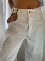 Pantalón de jean blanco de corte wide leg, con botón y cierre metálico color níquel. Presenta un recorte en la cadera con detalle de cadena metálica.